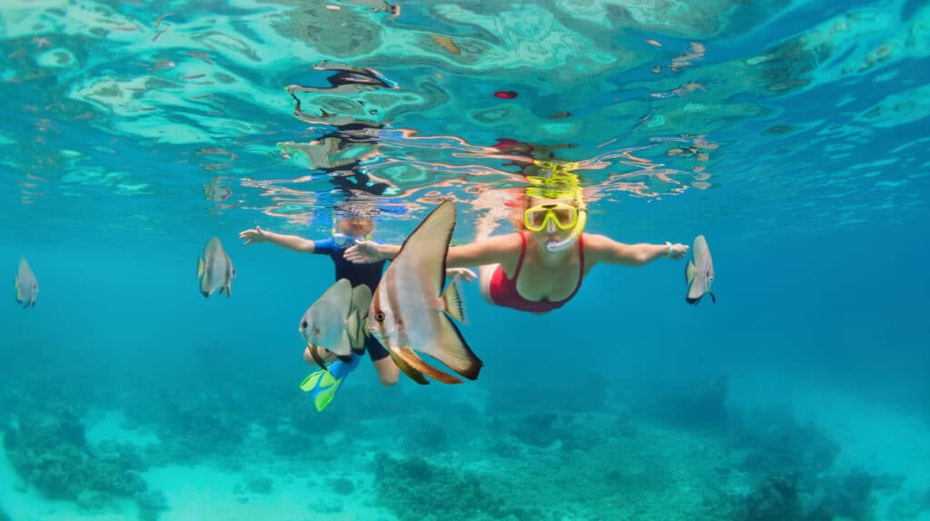 Mother, kid in snorkeling mask dive underwater with tropical fishes