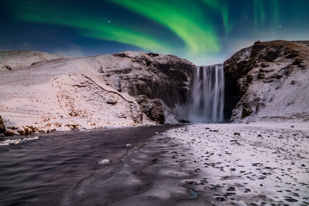 Skogafoss waterfall in the winter at night under the northern lights. Iceland